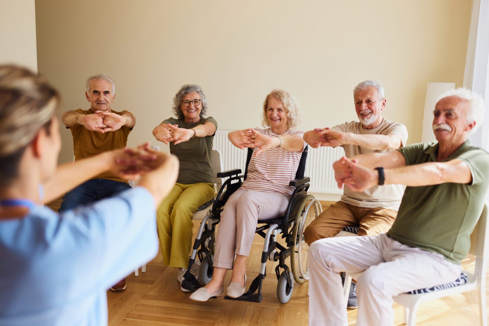 Happy disabled senior woman and her friends doing stretching exercises with their female nurse at retirement home.