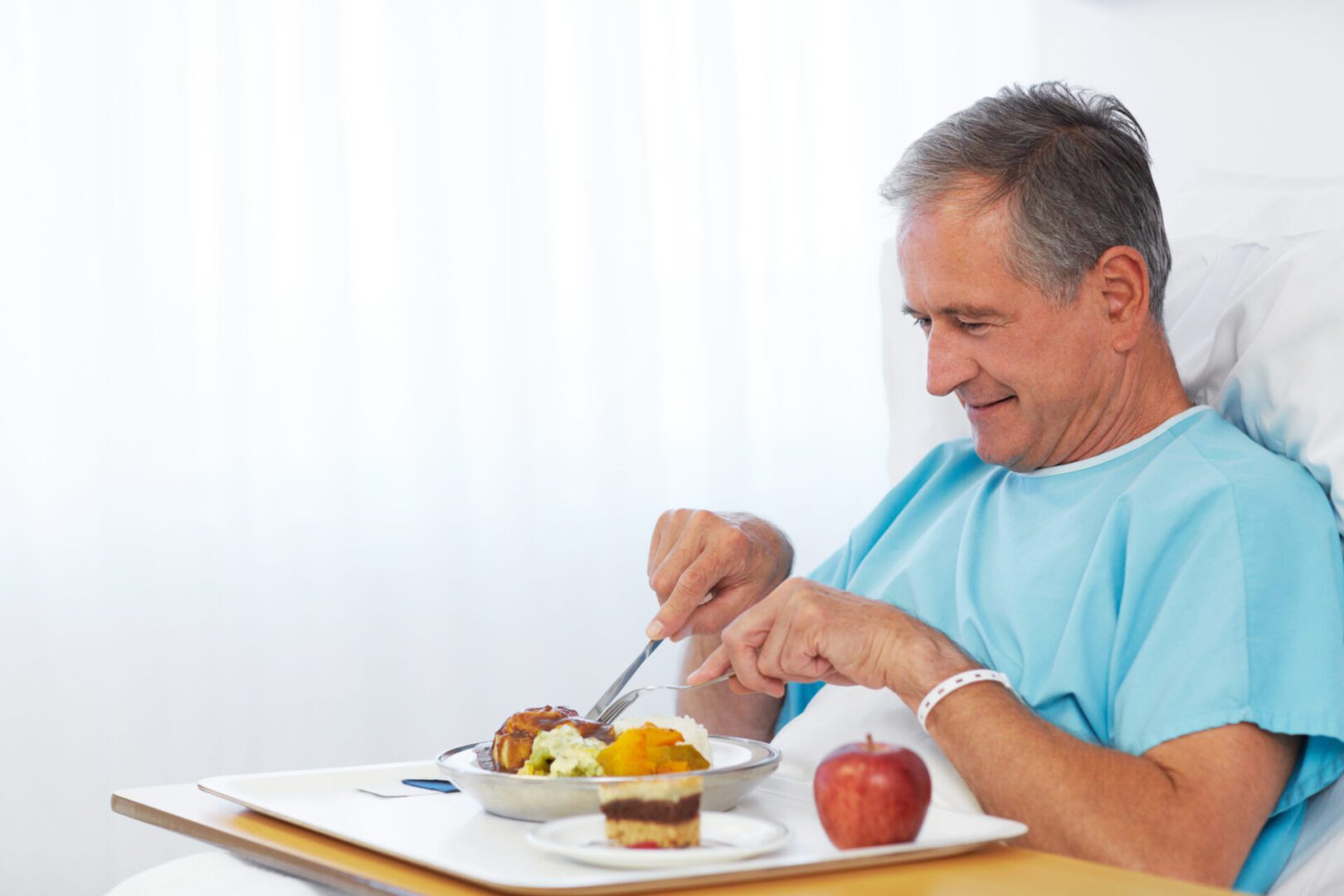 A happy senior man tucking into a healthy meal while recovering in hospital