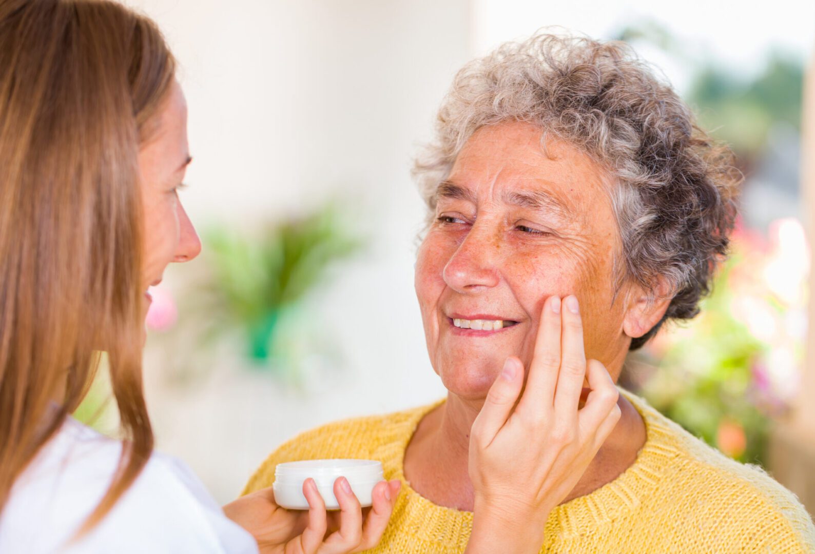 Caregiver rubs the face cream on the elderly womans face
